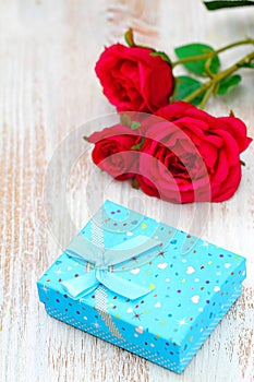 Fresh red roses and gift box on wooden table