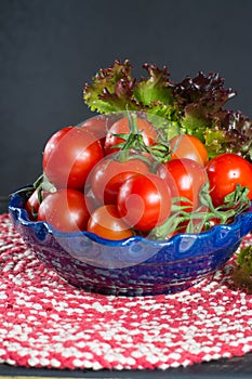 Fresh red small tomatoes and green leaf salad in blue bowl ready