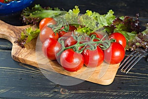 Fresh red small tomatoes and green leaf salad in blue bowl ready