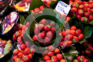 Fresh, red Strawberries in greenery at a local farmers market in Barcelona Spain. Counter with heap of berries.