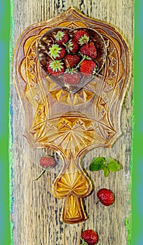 Fresh red strawberries in a heart-shaped wooden plate on a carved wooden kitchen board, on a green background