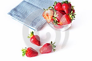 Fresh red strawberries in transparent bowl and small kitchen towel isolated on white background