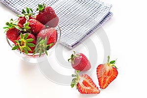 Fresh red strawberries in transparent bowl and small kitchen towel isolated on white background