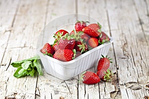 Fresh red strawberries in white bowl and mint leaves on rustic wooden background