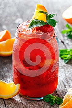 Fresh red strawberry lemonade with mint, orange and ice in glass jar on wooden background. Summer drinks and cocktails