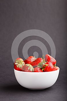 Fresh red strawberry in white bowl on black background. side view