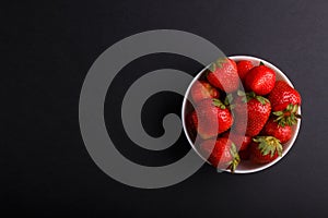 Fresh red strawberry in white bowl on black background. top view