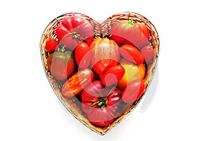 Fresh red and striped tomatoes in straw basket made in the shape of heart on white isolated background. The concept of