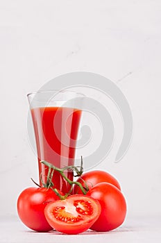 Fresh red tomato drink and pulpy tomatoes with juicy piece on light soft white wood table, copy space, vertical.