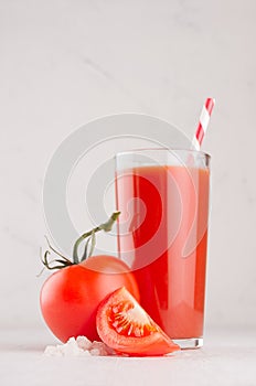 Fresh red tomato drink and pulpy tomatoes with juicy piece, straw, salt on light soft white wood table, vertical.