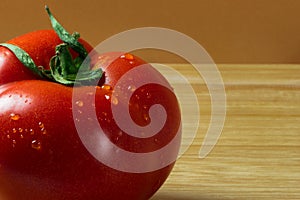 Fresh red tomato with drops of water on light brown wooden board as background.