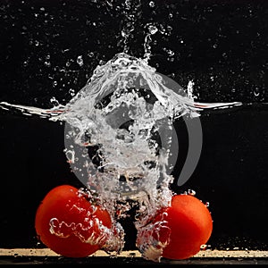 Fresh red tomato falling into water with water splash and air bubbles isolated on black background