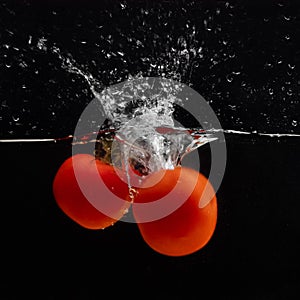 Fresh red tomato falling into water with water splash and air bubbles isolated on black background