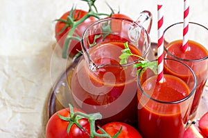 Fresh red tomato juice in a glass with a straw and jar with tomatoes on light wooden background.