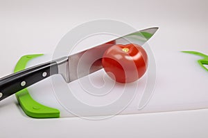A fresh red tomato and a large chef\'s knife lie on a cutting board