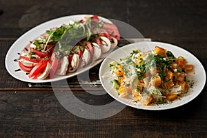 Fresh red tomato salad with feta and herbs on an oval white plate with yellow tomato salad with green onions on a dark wooden back