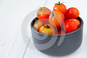 Fresh red tomatoes in black bowl on white wooden table