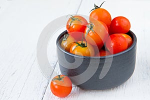 Fresh red tomatoes in black bowl on white wooden table