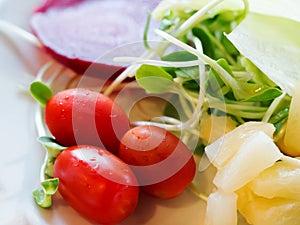 Fresh red tomatoes with green vegetable and beetroot, pineapple in white plate for salad meal. Clean and healthy food concept.