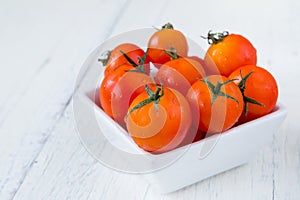 Fresh red tomatoes in white bowl on white wooden table