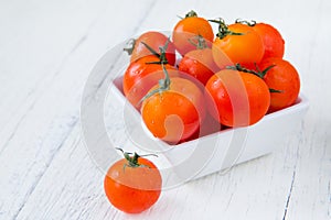 Fresh red tomatoes in white bowl on white wooden table