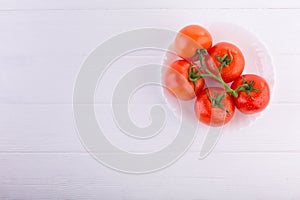 Fresh red tomatoes on a white plate at a white table shot from the top