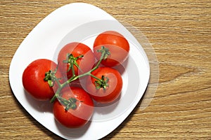 Fresh red tomatoes in white plate on wooden table