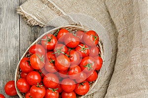 Fresh red tomatoes in a wicker basket on an old wooden table. Ripe and juicy cherry tomatoes with drops of moisture