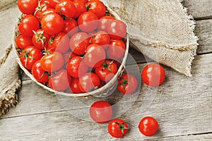 Fresh red tomatoes in a wicker basket on an old wooden table. Ripe and juicy cherry tomatoes with drops of moisture, gray wooden