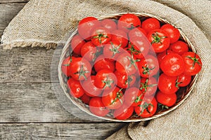 Fresh red tomatoes in a wicker basket on an old wooden table. Ripe and juicy cherry tomatoes with drops of moisture, gray wooden