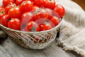 Fresh red tomatoes in a wicker basket on an old wooden table. Ripe and juicy cherry tomatoes with drops of moisture, gray wooden