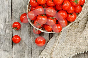 Fresh red tomatoes in a wicker basket on an old wooden table. Ripe and juicy cherry tomatoes with drops of moisture, gray wooden