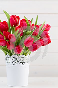 Fresh red tulip flowers bouquet on shelf in front of wooden wall