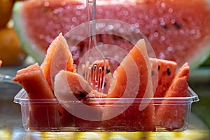 Fresh red watermelon fruit cut in tray ready to eat with clear fork selling in local market blurred background, selective focus