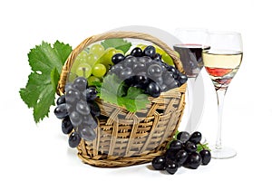 Fresh Red and White Grapes with Green Leaves in Wicker Basket and Two Wine Glass Cups Filled with Red and White Wine Isolated