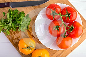 Fresh red and yellow tomatoes from above on a wooden board with a knife in a white plate at a white table