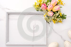 Fresh red and yellow tulips flowers bouquet, blank photo frame and eggs on white wooden background on white marble background. Spr