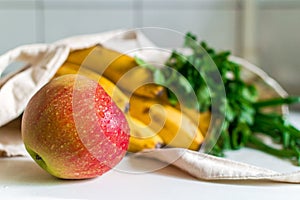 Fresh ripe apple, bunch of parsley and green onion, bananas and French baguette in canvas reusable grocery tote bag on the kitchen