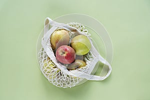 Fresh ripe apples in a string bag on green background. Zero waste, no plastic concept. Top view, flat lay