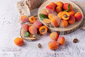 Fresh ripe apricots and mint leaves on wooden tray.  Whole and slices organic apricot fruits  scattered on light stone background