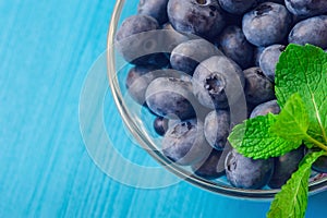 Fresh ripe blueberries with leaves in bowl on blue wooden planks