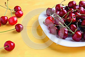 Fresh ripe cherries in a bowl with water drops, yellow background