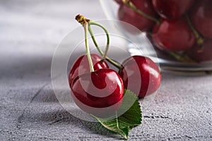 Fresh ripe cherry branch near to cherries with green leaves in glass bowl, summer vitamin berries