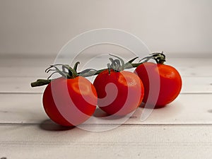 Fresh ripe cherry tomatoes on a green branch on a background of light wooden boards