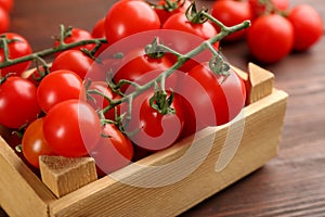 Fresh ripe cherry tomatoes in wooden crate on table, closeup