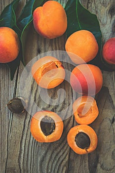 Fresh ripe colorful apricots halved and whole on weathered plank wood background, kernel, green leaves matte filter