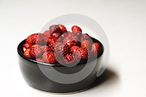 Fresh ripe dark red wild strawberries in a black bowl on a white background