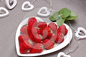 Fresh ripe delicious red strawberries and green mint leaf on a white heart-shaped plate. Harvest. beautiful bright berries