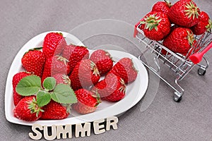 Fresh ripe delicious red strawberries and a green mint leaf on a white heart-shaped plate. The word SUMMER. Harvest