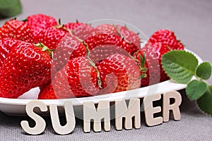 Fresh ripe delicious red strawberries and a green mint leaf on a white heart-shaped plate. The word SUMMER. Harvest